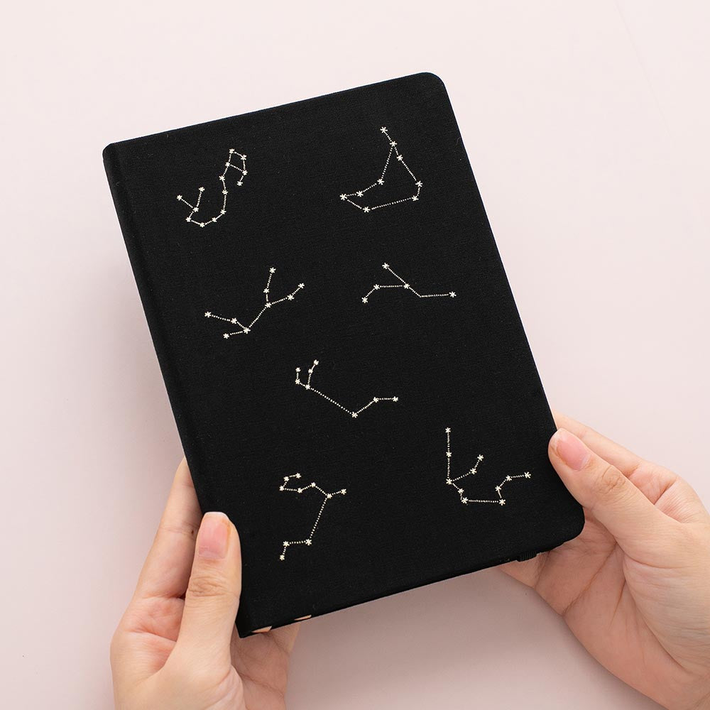 Hands holding tsuki constellations bullet journal in deep black
