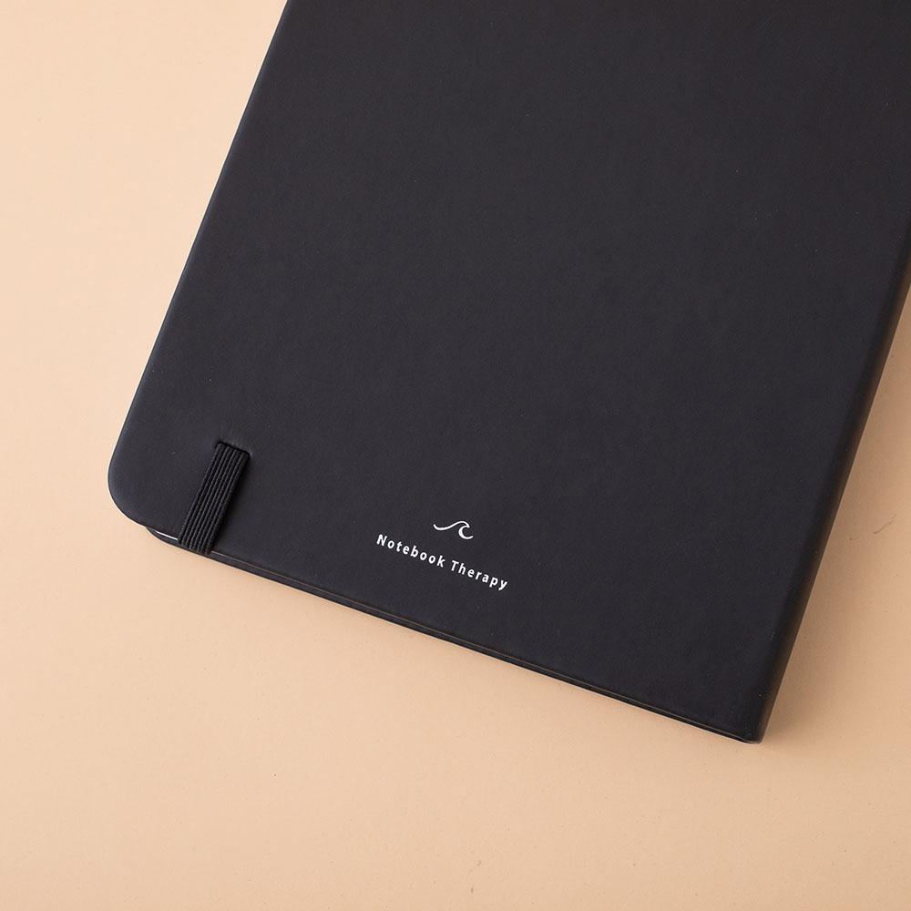 Close up of the back cover of deep black Tsuki Playful Orca limited edition bullet journal on peach background