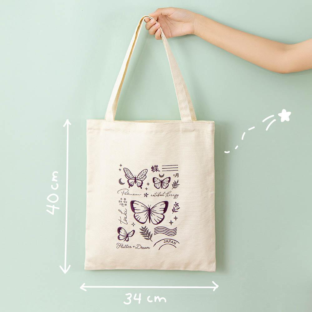 Tsuki ‘Flutter + Dream’ Tote Bag by Notebook Therapy x Pelinkan measuring 34cm by 40cm held in hand in mint background 