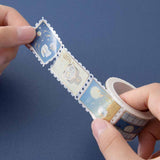 Close up of Tsuki ‘Moonlit Wish’ Stamp Washi Tape held in hands in dark blue background