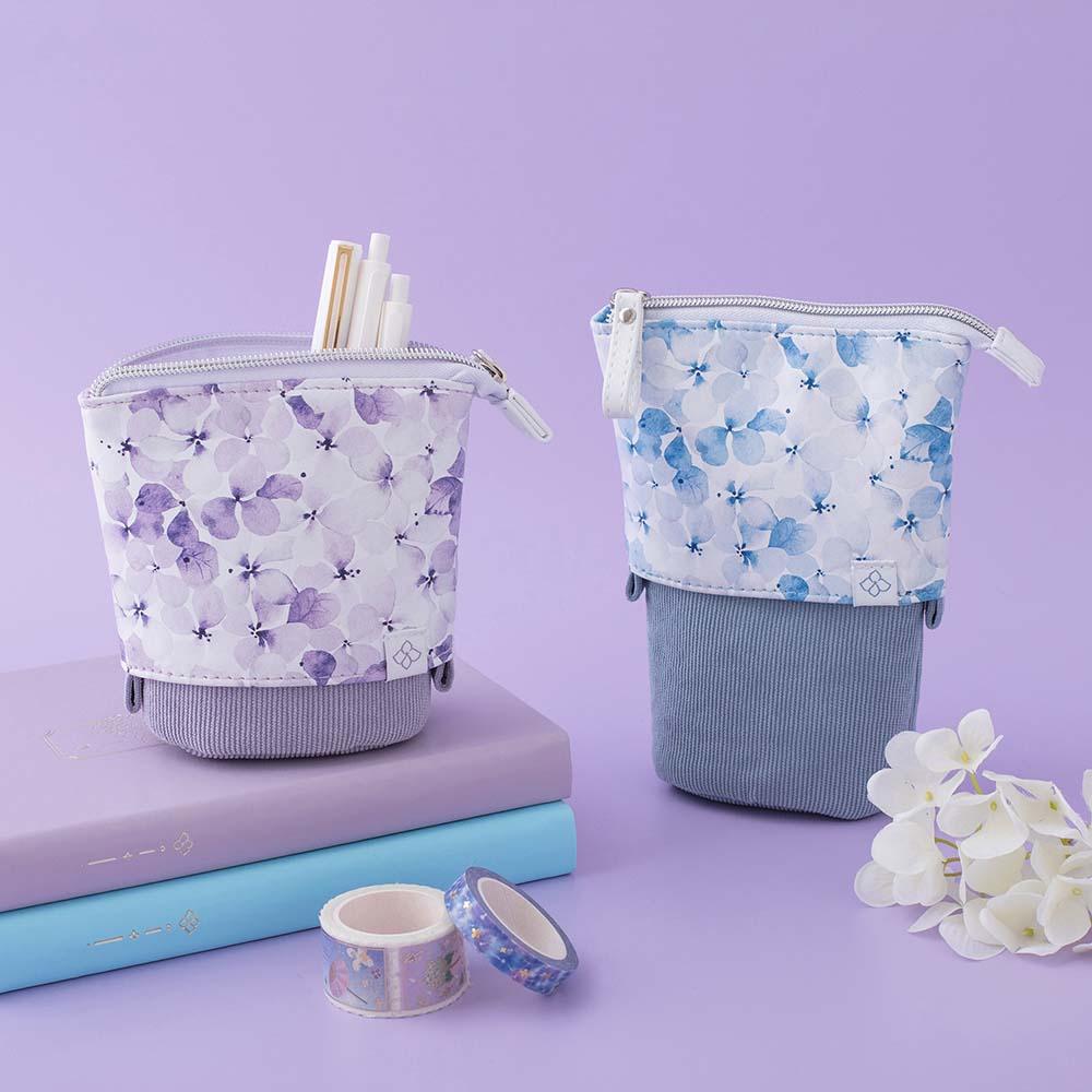 Tsuki Endless Summer Pop-Up Pencil cases in Lilac Bloom and Petal Blue with Tsuki Endless Summer Washi Tape rolls and Tsuki Endless Summer Limited Edition Bullet Journals with white hydrangea flowers in lilac background