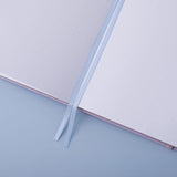 Close up of open pages of Tsuki Endless Summer Limited Edition Bullet Journal with two bookmark ribbons on light blue background