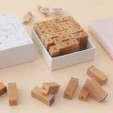 Close up of Tsuki Bullet Journal Typewriter Style Alphabet Stamps with eco-friendly gift box packaging at an angle on beige background