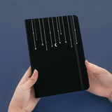 Tsuki Black Paper Limited Edition Hardcover Bullet Journal in Falling Star held in hands in navy background