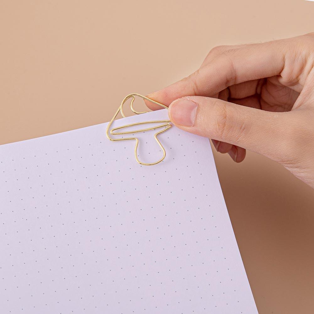 Close up of open page of Tsuki ‘Kinoko’ Limited Edition Bullet Journal with free paperclip gift held in hand on beige background