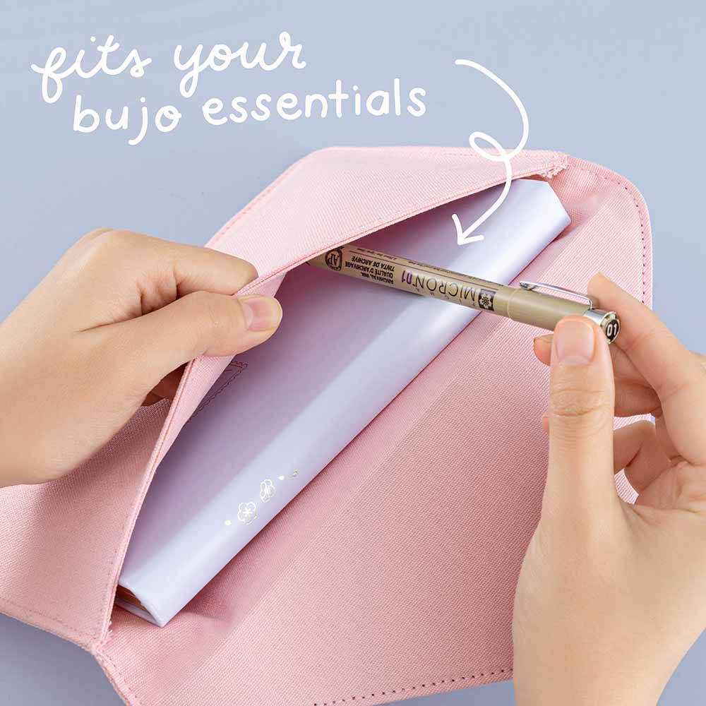 Open Tsuki ‘Sakura Journey’ Notebook Pouch with pen held in hands with original size Tsuki ‘Sakura Journey’ Limited Edition Bullet Journal inside in light blue background