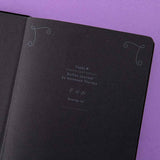 Close up of open front page of Tsuki ‘Moonlit Spell’ Limited Edition Holographic Bullet Journal with black paper on purple background