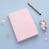 Tsuki ‘Lunar Blossom’ Limited Edition Bullet Journal with free bookmark gift with Tsuki ‘Sakura Journey’ Washi Tape Set with pen and cherry blossom petals on light blue background