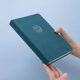 Tsuki sea green velvet Dolphin Days notebook held in hands in blue background