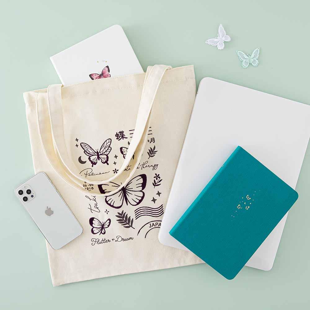 Tsuki ‘Flutter + Dream’ Tote Bag by Notebook Therapy x Pelinkan with Tsuki Teal Sky ‘Flutter + Dream’ Limited Edition Bullet Journal by Notebook Therapy x Pelinkan and Tsuki Cloud White ‘Flutter + Dream’ Limited Edition Bullet Journal by Notebook Therapy x Pelinkan with laptop and mobile phone and butterflies on mint background