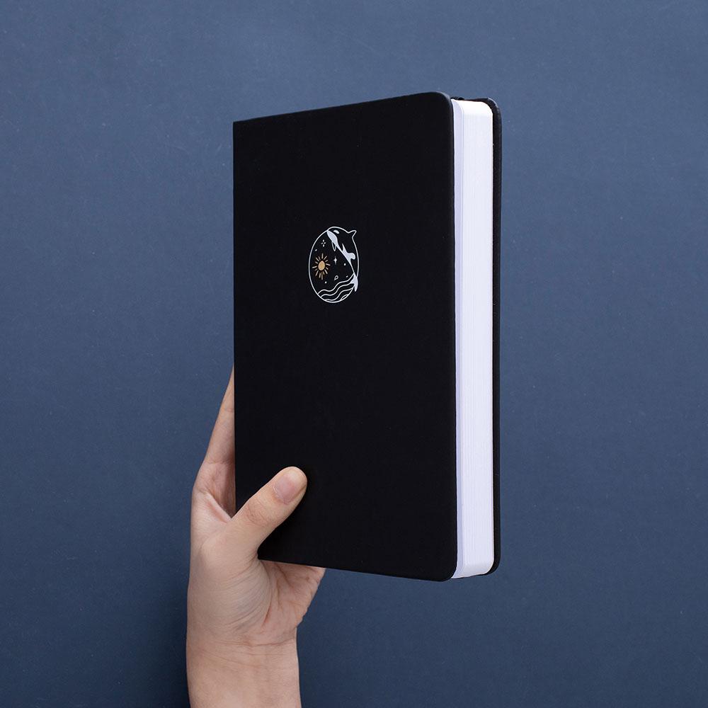 Tsuki deep black Playful Orca limited edition notebook held in hand at an angle in dark blue background
