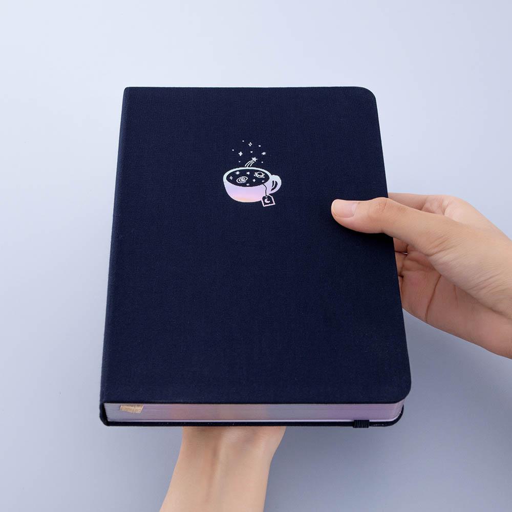 Tsuki ‘Cup of Galaxy’ Limited Edition Holographic Bullet Journal held in hands at an angle in light blue background