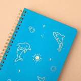 Close up of Tsuki Ocean Edition Ring Bound notebook in aqua blue on peach background