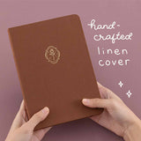 Tsuki ‘Vintage Rose’ Limited Edition Bullet Journal with handcrafted linen cover held in hands in mauve background