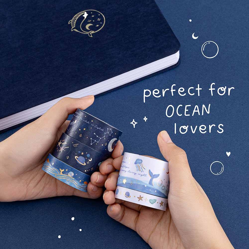 Hands holding rolls of ocean-themed washi tapes with a deep blue velvet gentle giant bullet journal in the background and the words ‘perfect for ocean lovers’ written in white