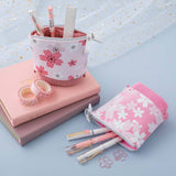 Tsuki 'Sakura Edition' Pop-Up Pencil Case in blush pink and petal pink with pens inside on Tsuki 'Sakura' Limited Edition Bullet Journal in blush pink and petal pink with free bookmark gifts and Tsuki 'Sakura Edition' Washi Tapes on sparkly netting on light blue background