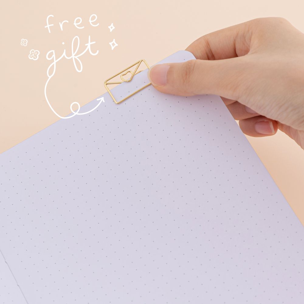 Hand putting love letter-shaped paperclip in gold on a bullet journal page with the words ‘free gift’ in white lettering