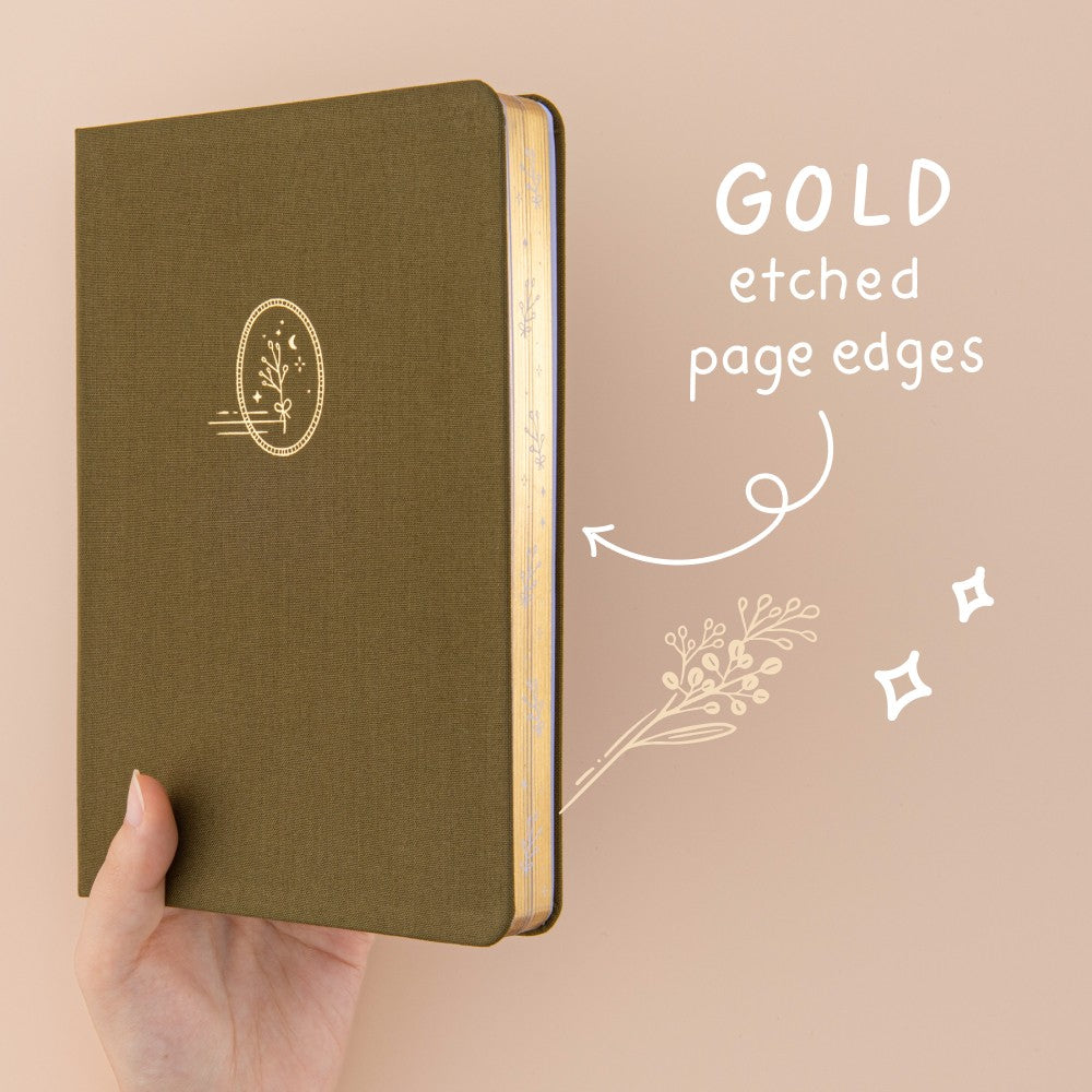 Hand holding up green linen bullet journal with gold gilded page edges