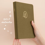 Hands holding up a green bullet journal with the words ‘gold details’ in white lettering