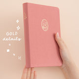 Hands holding up a pink cat bullet journal with the words ‘gold details’ in white lettering