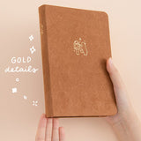 Hands holding up a brown bear bullet journal with the words ‘gold details’ in white lettering