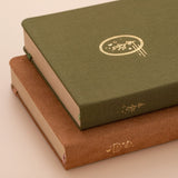 Tsuki Mori green linen bullet journal and Kuma brown velvet bullet journal stacked on top of each other