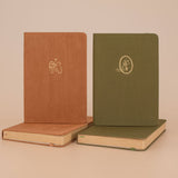 Tsuki Kuma brown velvet bullet journal and tsuki mori green linen bullet journal next to each other