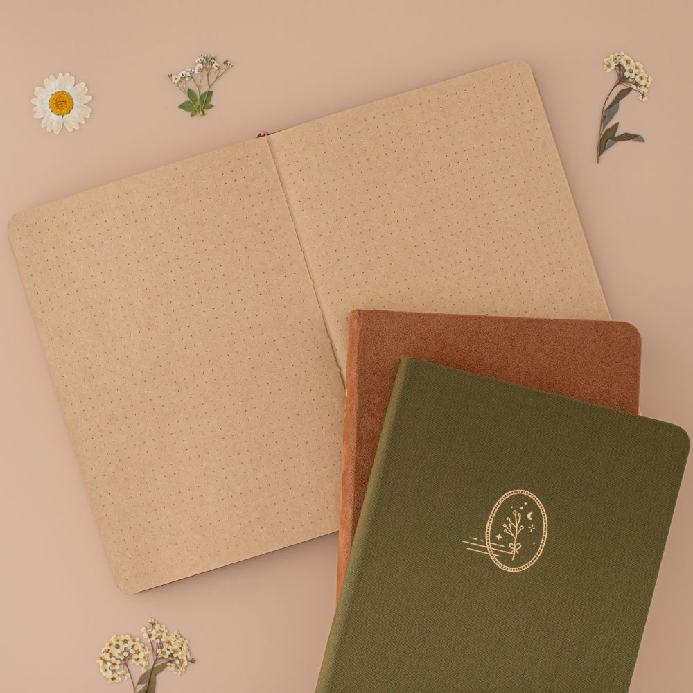 Kraft paper bullet journal laid flat with brown velvet notebook and green linen notebook on top