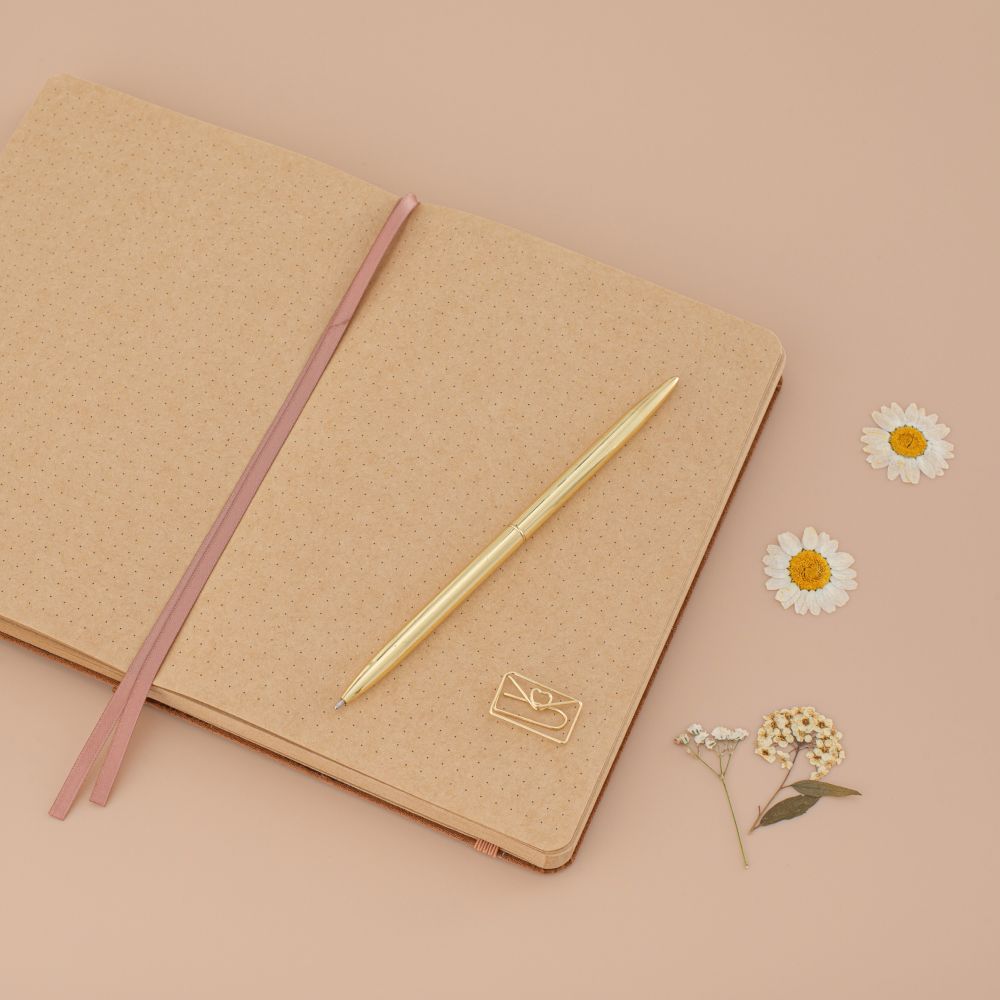 Kraft paper bullet journal laid flat with gold pen and gold love letter shaped paperclip on top