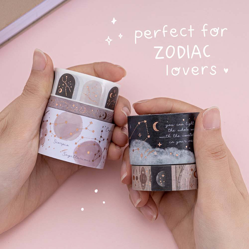 A pair of hands holding Constellations washi tape rolls on pink background with white text that says “perfect for ZODIAC lovers”