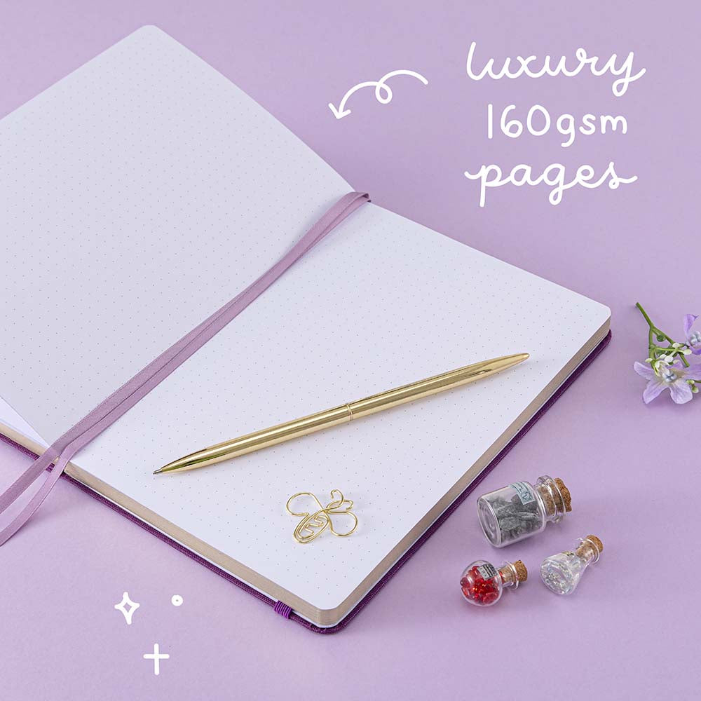 Tsuki ‘Enchanted Garden’ lavender foil design on purple linen bullet journal on purple background with white text saying ‘luxury 160gsm pages’