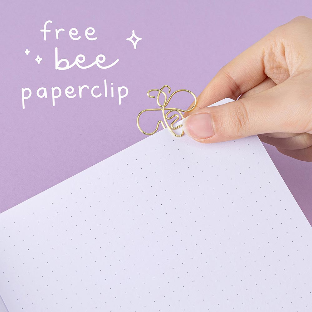 Tsuki ‘Enchanted Garden’ lavender foil design on purple linen bullet journal on purple background with white text saying ‘free bee paper clip’