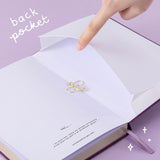 Tsuki ‘Enchanted Garden’ lavender foil design on purple linen bullet journal on purple background with white text saying ‘back pocket’