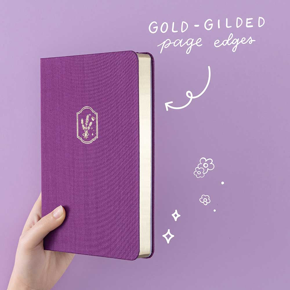 Tsuki ‘Enchanted Garden’ lavender foil design on purple linen bullet journal on purple background with white text saying ‘gold-gilded page edges’
