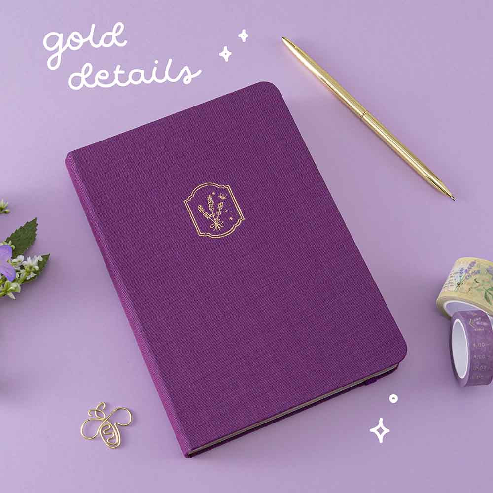 Tsuki ‘Enchanted Garden’ lavender foil design on purple linen bullet journal on purple background with white text saying ‘gold details’