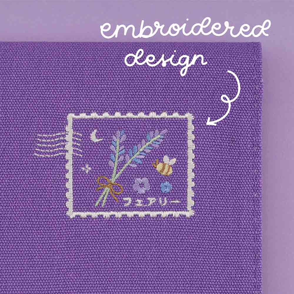 Close up of embroidered design at the back of the notebook pouch featuring lavender, bee, crescent moon and some Japanese text in a stamp shape