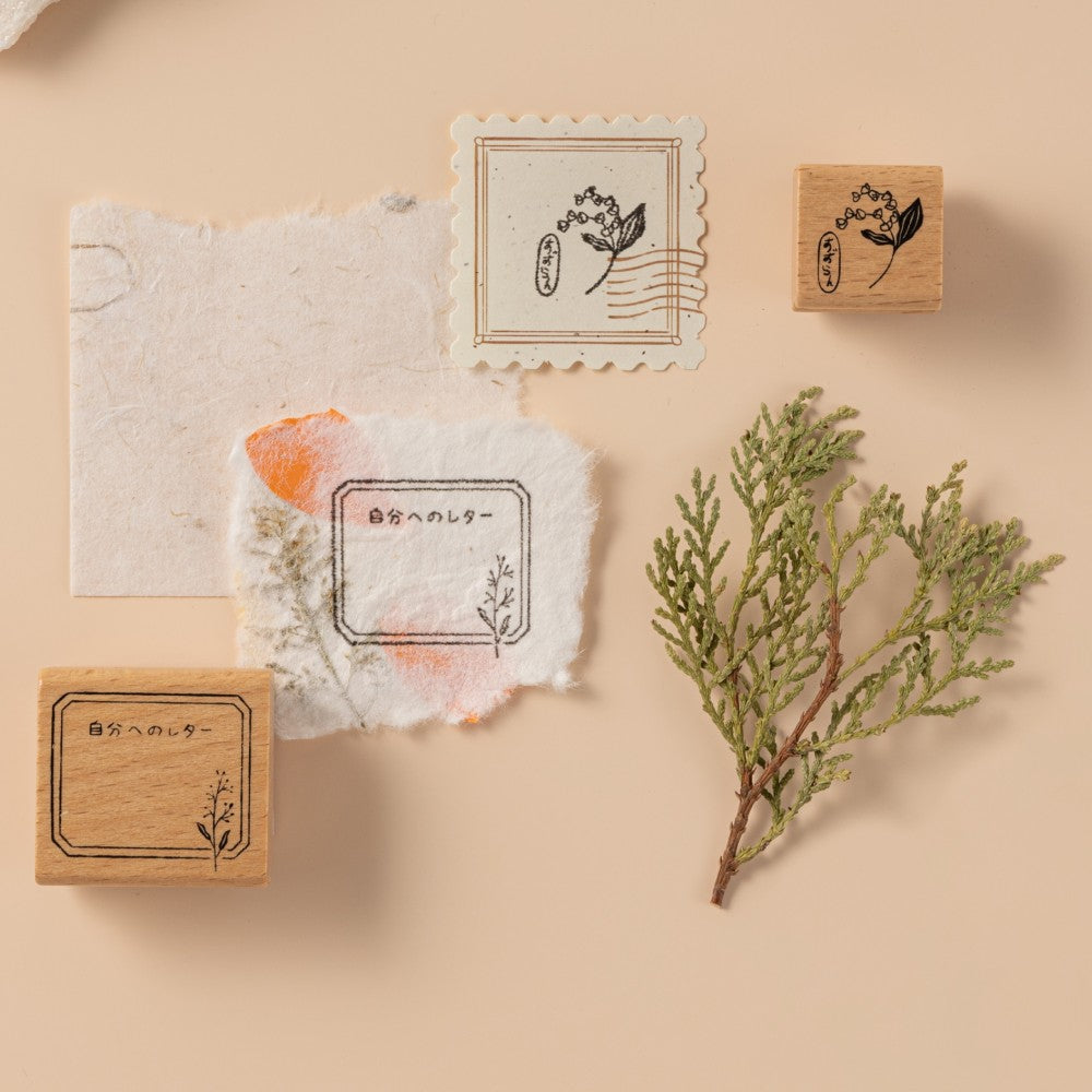 Close up of two stamps stamped on textured paper on beige background with pine leaf as decoration