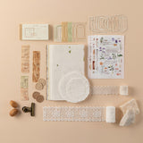 Flatlay of contents of Hinoki Scrapbook Ephemera Starter Set including textured paper, sticker sheets, lace, doilies, train ticket stickers, wax seal stickers, paper frames, gold clip and a label book