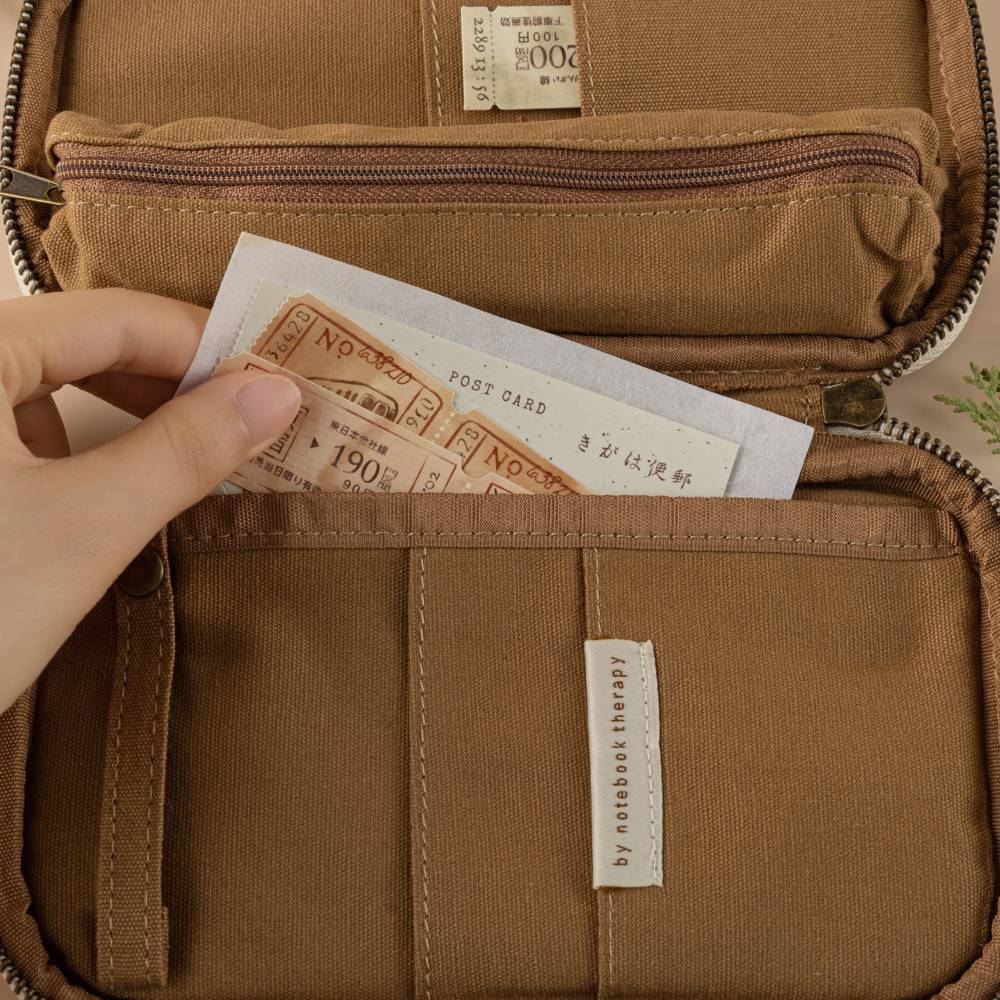 Hand putting tickets and postcards inside the larger pocket of the brown pencil case