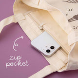 Close up of a tote bag with a zip pocket and a phone inside the pocket with the words “zip pocket” written in white