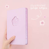 Tsuki Four Seasons: Spring Collector’s Edition 2022 Bullet Journal with illustrated page edges held in hand in light pink background