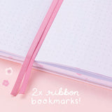 Close up of open Tsuki Four Seasons: Spring Collector’s Edition 2022 Bullet Journal with two bookmark ribbons on light pink background