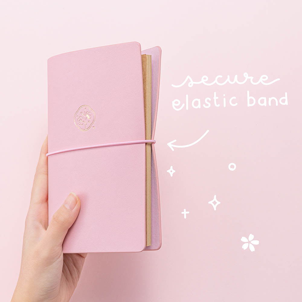 Tsuki ‘Sakura Journey’ Limited Edition Travel Notebook with secure elastic band closure held in hands in pink background