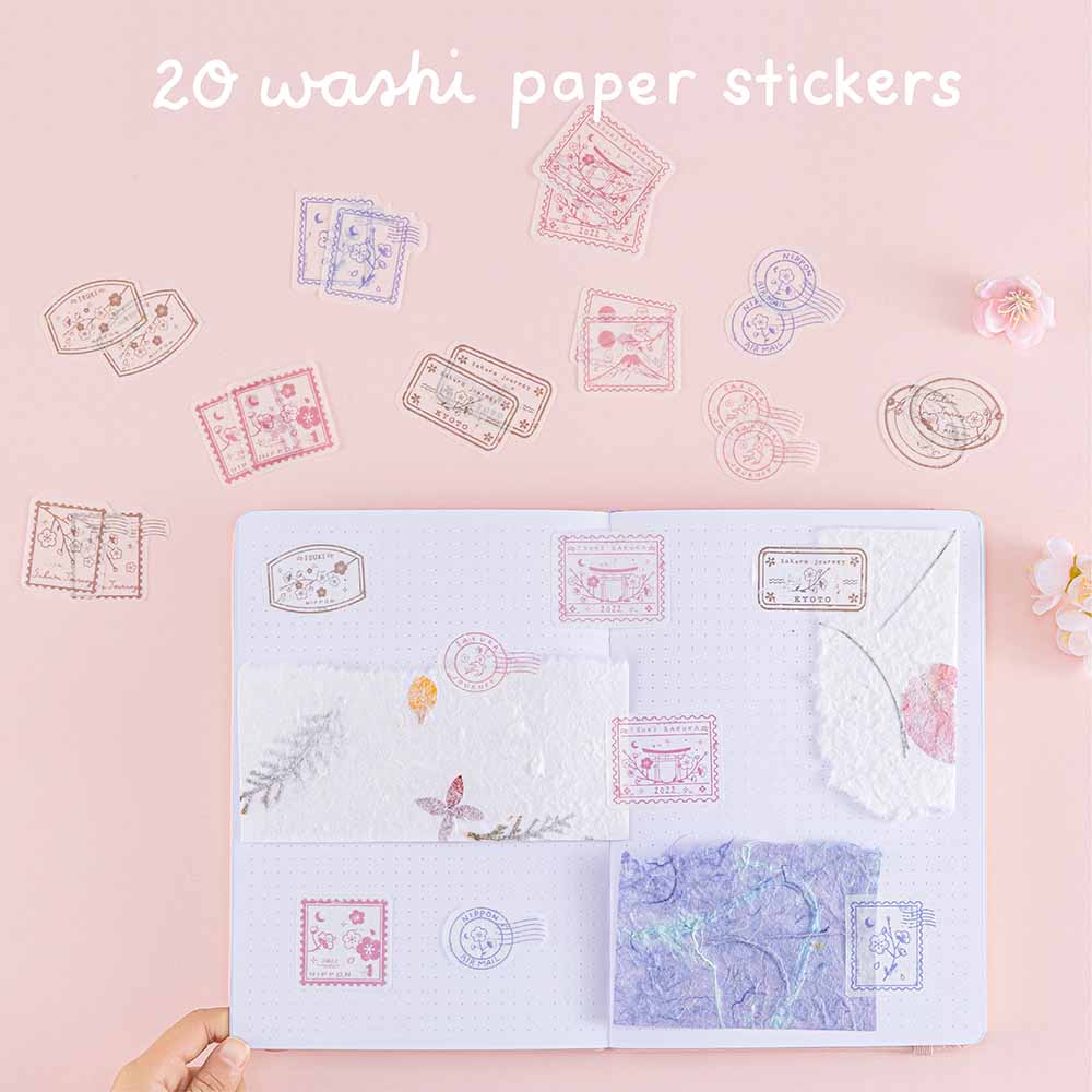 Twently washi stickers from Tsuki ‘Sakura Journey’ Scrapbooking Set on Tsuki ‘Sakura Journey’ Limited Edition Travel Notebook held in hand in pink background