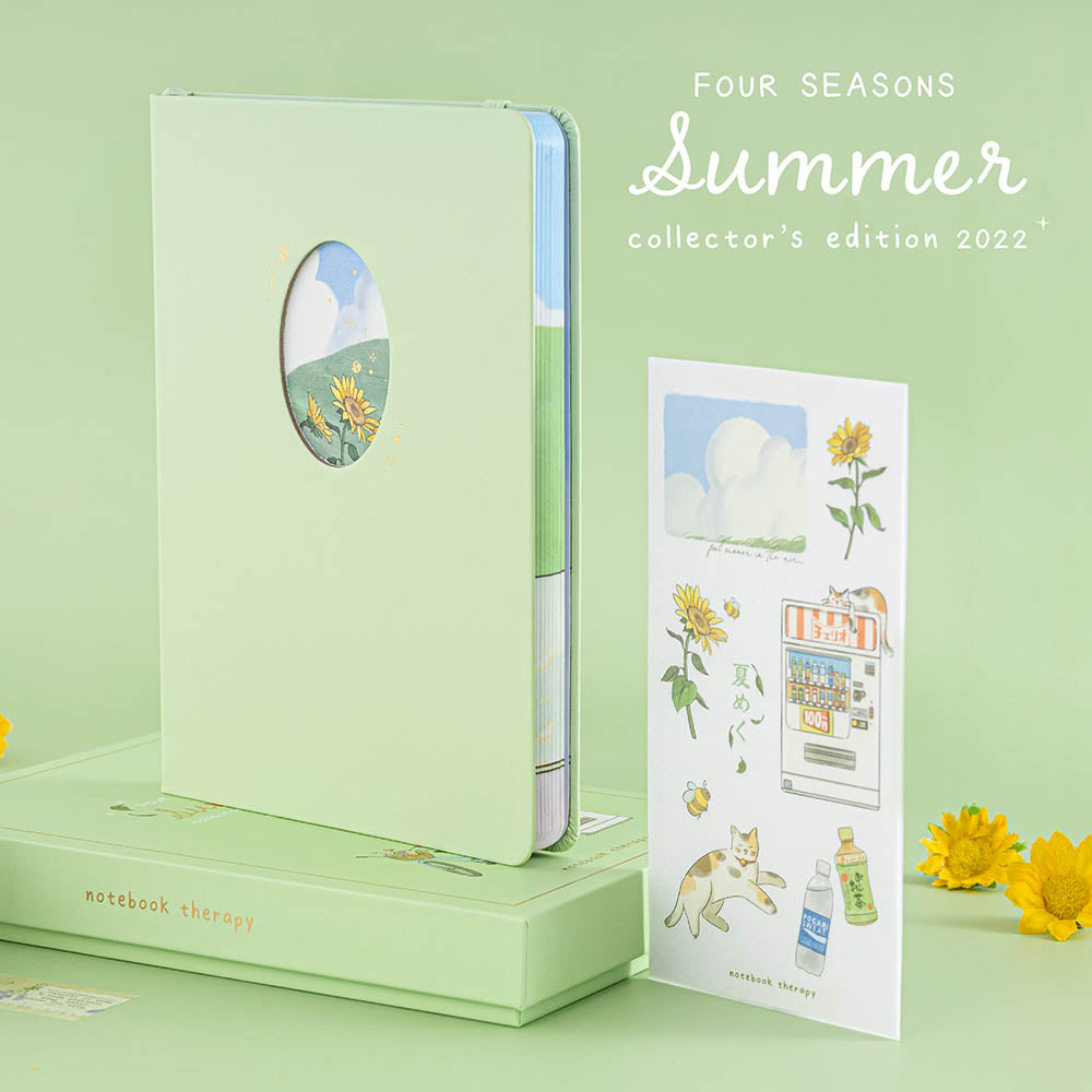 Photo of Tsuki Four Seasons Summer Collectors Edition 2022 sage bullet journal notebook standing on the gift box and the sticker sheet stood upright