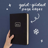 Tsuki ‘Winter Journey’ Limited Edition Bullet Journal with gold gilded page edges held in hand in navy background