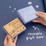 Tsuki ‘Dreams of Snow’ Bullet Journal Stamp Set with reusable gift box held in hands with snowflakes in navy background