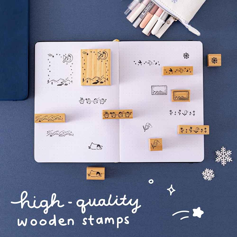 Tsuki ‘Dreams of Snow’ Bullet Journal Stamp Set with high quality wooden stamps on open bullet journal spread with Tsuki ‘Winter Wishes’ Limited Edition Bullet Journal Spread and Tsuki ‘Dreams of Snow’ Pop-Up Pencil Case in Playful Penguin with snowflakes on navy background